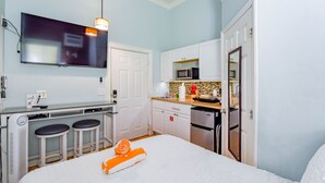 Ein kleines Hotelzimmer mit Küchenzeile, einem Bett und einem orangefarbenen Handtuch, einem Fernseher und einer Mikrowelle.