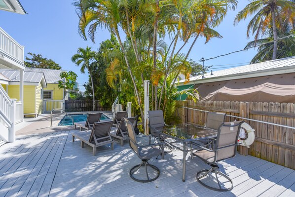 A wooden deck with a glass-top table and chairs, a pool, and palm trees. - VanGogh Studio | Updated, Old Town, Heated Pool (Key West)
