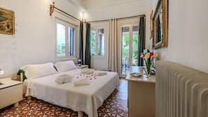 A hotel room with a bed, a desk, a radiator, and a view of greenery outside.