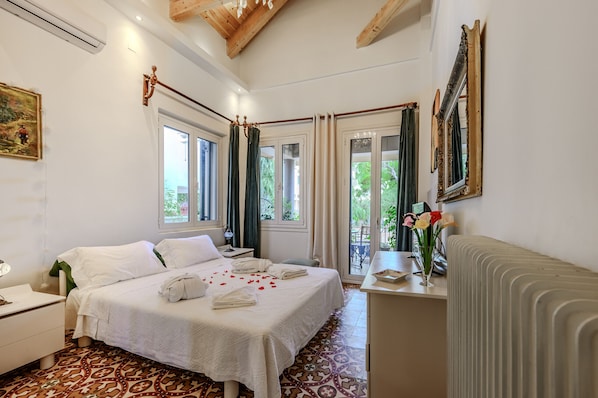 A hotel room with a bed, a desk, a radiator, and a view of greenery outside.