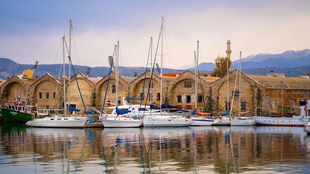 A marina with several sailboats docked in front of a historic building with arched windows and a bell tower.