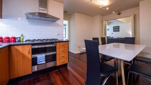 Cocina moderna con estufa a gas, horno y campana extractora de acero inoxidable. Hay un comedor con mesa blanca y sillas negras.