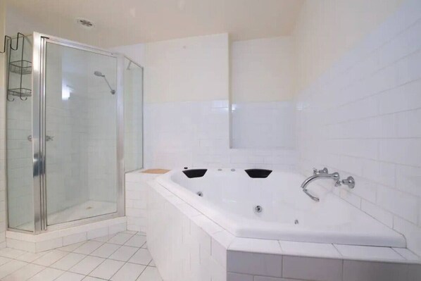 Un baño moderno con ducha envuelta en vidrio, una bañera independiente grande y paredes de azulejos blancos.