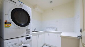 Un área de lavandería con lavadoras y secadoras apiladas, un lavabo y una encimera.