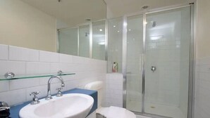 Un baño con ducha envuelta en vidrio, un lavabo blanco y un inodoro.