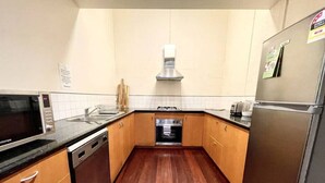 A compact kitchen with wooden cabinets, a stainless steel refrigerator, a microwave, and a dishwasher. - Spacious 2BR Apartment with Extra Sleeping Space (Melbourne)