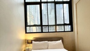 A hotel room with a large window, a bed with white linens, and a nightstand with a lamp. - Spacious 2BR Apartment with Extra Sleeping Space (Melbourne)