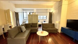 A spacious living room with a sofa set, a coffee table, and a television. - Spacious 2BR Apartment with Extra Sleeping Space (Melbourne)