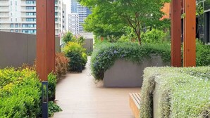 A wooden pathway leading to a covered area with greenery and a bench. - Lonsdale Heights (Higher Floor) 1BR with City View (Melbourne)