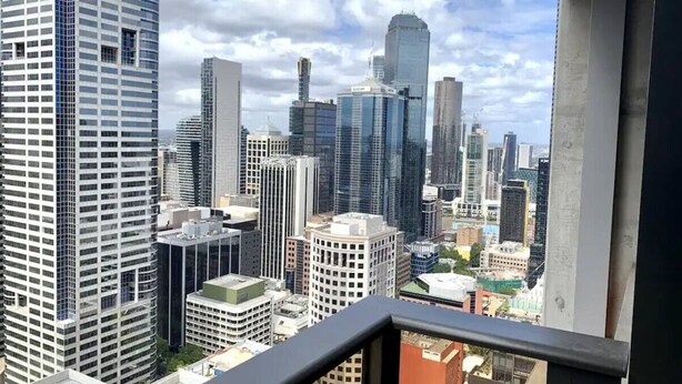A cityscape with high-rise buildings, including a prominent skyscraper with a unique design. - Lonsdale Heights (Higher Floor) 1BR with City View (Melbourne)