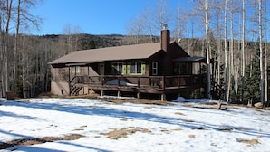 A cabin with a deck, surrounded by a snowy landscape and trees.