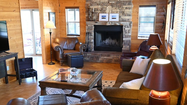A cozy log cabin interior with a stone fireplace, leather furniture, and a television.