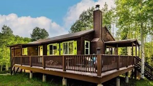 A wooden cabin with a deck, surrounded by trees.