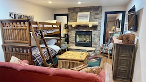 A cozy living room with a bunk bed, fireplace, and a red sofa.