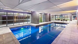 Ein moderner, überdachter Pool mit klaren Glaswänden, gefliestem Boden und einer Decke mit geometrischen Mustern.