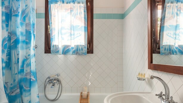 A bathroom with a bathtub, a sink, and a window with a curtain. - Apartments With Pool Country Village (Stintino)