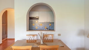 A dining area with a table, chairs, and a view of a kitchen through an arched window. - Apartments With Pool Country Village (Stintino)