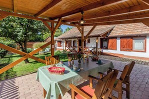 A covered outdoor dining area with a table set for two, surrounded by wooden chairs.