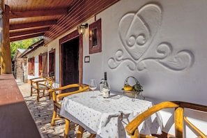 Un espace extérieur abrité, aménagé pour les repas, avec des tables et des chaises en bois, une nappe blanche et un mur décoratif.