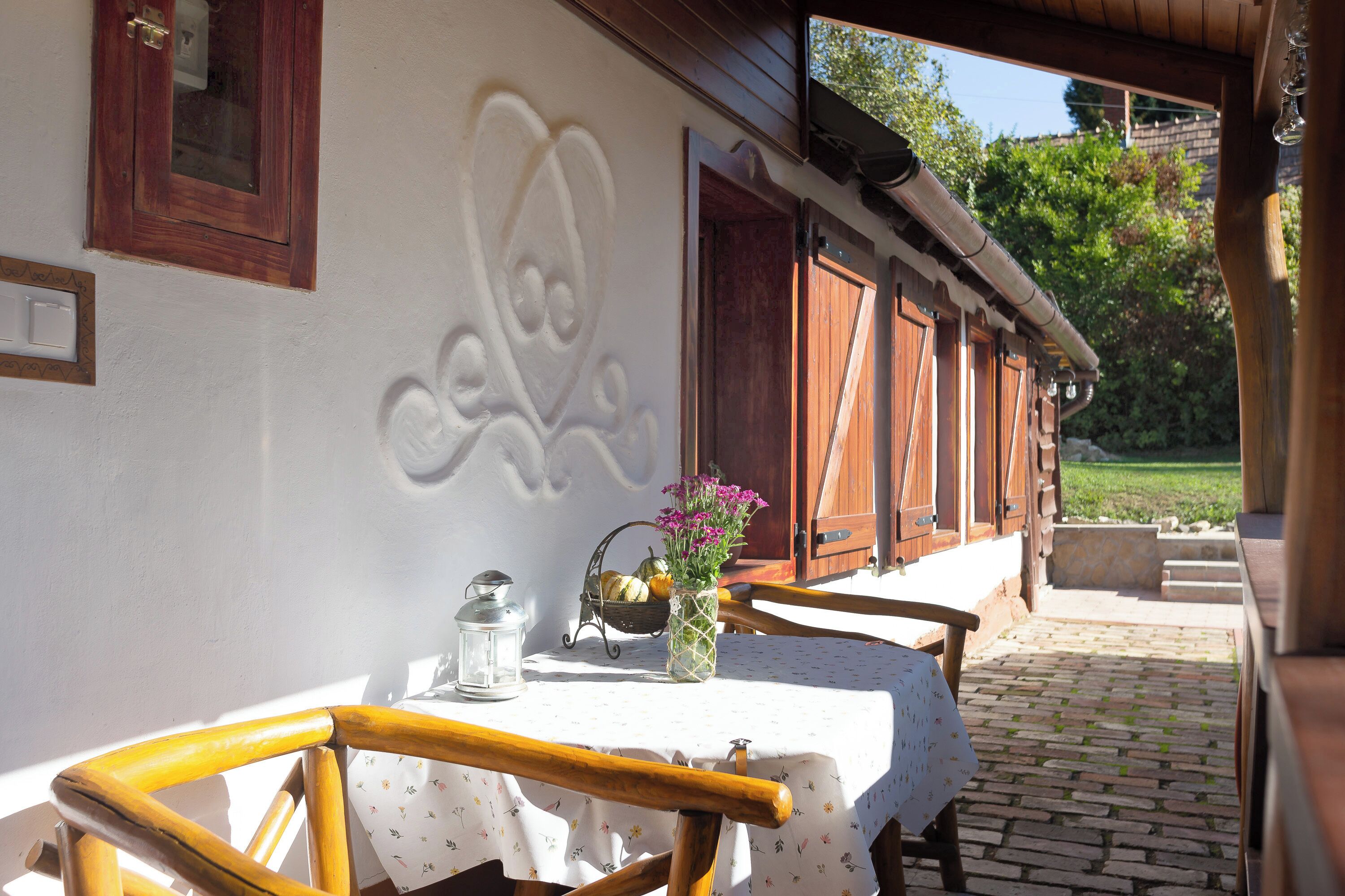 A patio with a table set for dining, a vase with flowers, and a lantern.