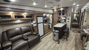 Interior compacto de autocaravana con cocina americana, sofá de cuero y una pequeña zona de comedor.