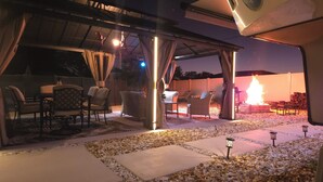 Un patio al aire libre con mobiliario, una fogata y una pérgola.