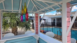 Un espacio de estar al aire libre cubierto con vista a la piscina, con una palmera y botellas colgantes de colores.