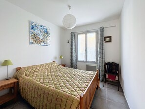 A bedroom with a large bed, a bedside table, a lamp, a window with curtains, and a painting on the wall.