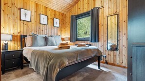 A wooden-paneled bedroom with a bed, two bedside tables, a window with curtains, and a mirror. - Newsham Lodge (Penrith)