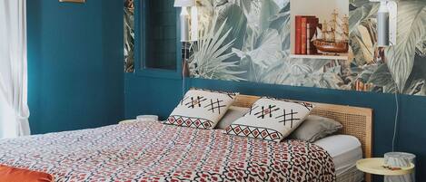 A bedroom with a teal wall, a patterned bedspread, a wooden headboard, a small bedside table, and a mirror.