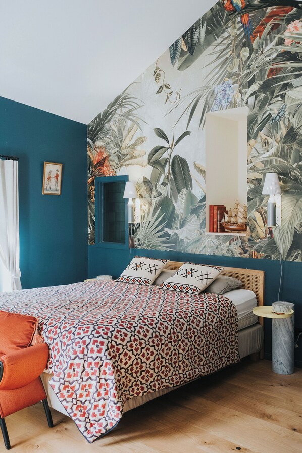 A bedroom with a teal wall, a patterned bedspread, a wooden headboard, a small bedside table, and a mirror.