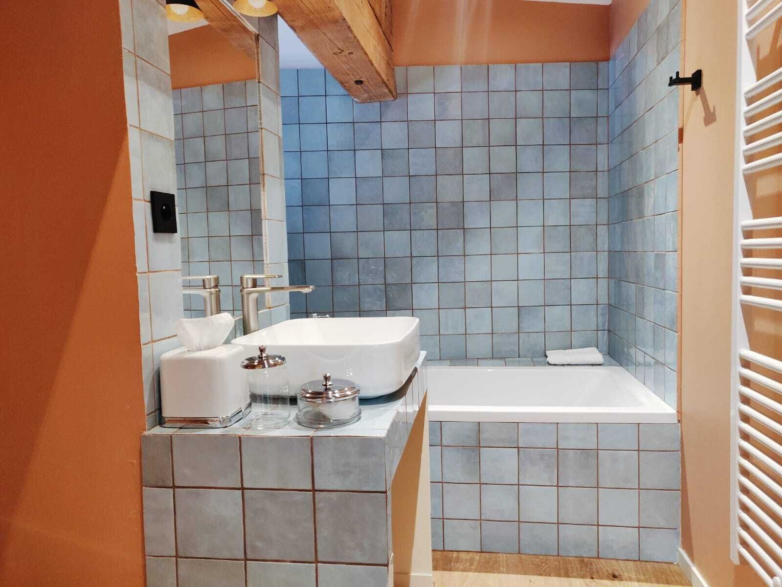 Ein Badezimmer mit einer weißen Badewanne, einem Waschbecken mit Spiegel und einer gefliesten Duschkabine.