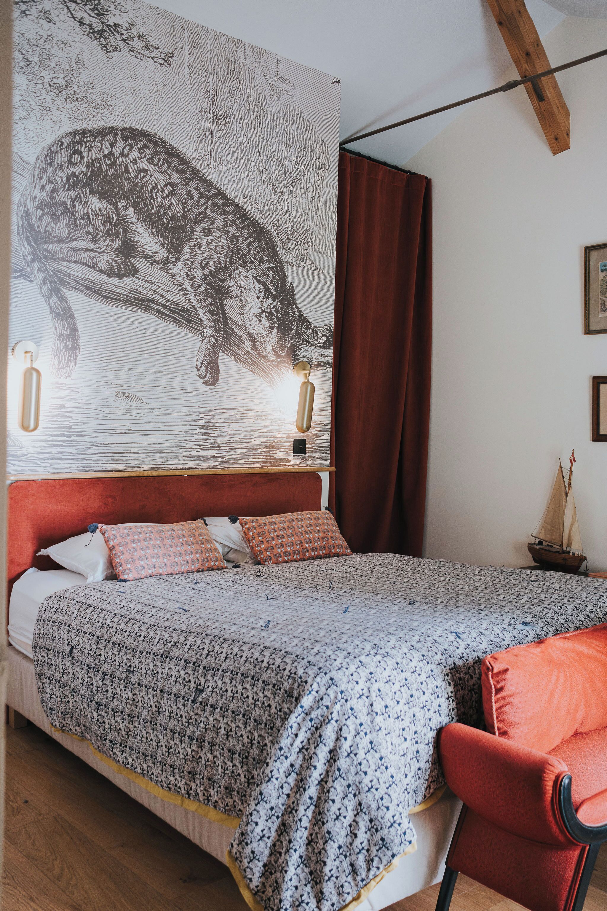 Ein Schlafzimmer mit einem großen Bett, einem roten Sessel, einem Holzbalken an der Decke und einer Wandleuchte.