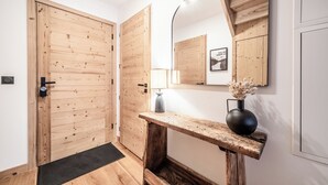A hallway with wooden doors, a black doormat, a wooden console table with a vase, and a wall-mounted mirror. - Gentiana - Cosy apartment in Les Gets (Les Gets)