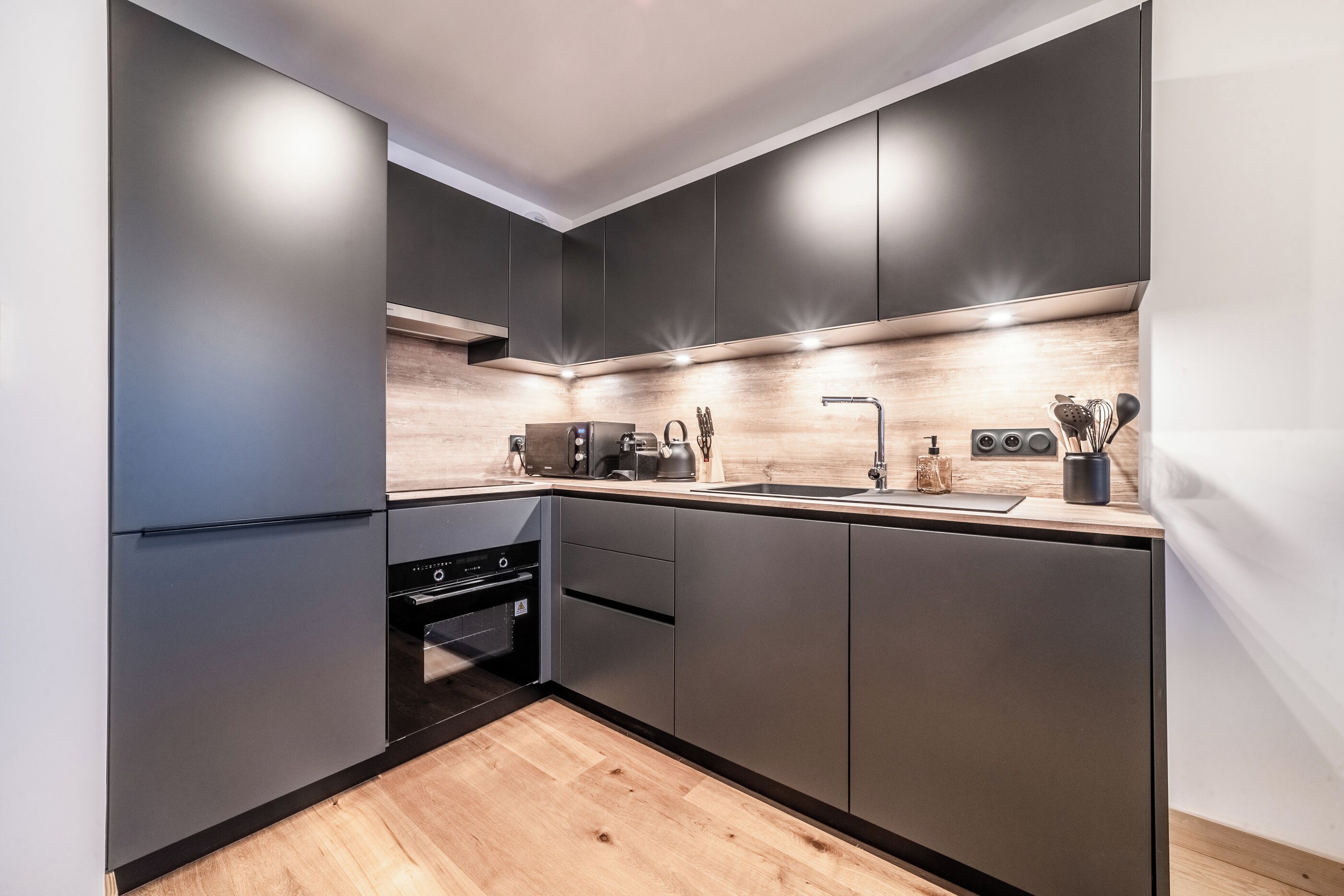 Une cuisine moderne avec des meubles de couleur sombre, un plan de travail en bois et des appareils électroménagers intégrés.