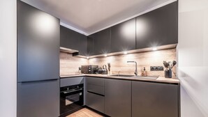 A modern kitchen with dark cabinets, a wooden countertop, and built-in appliances. - Gentiana - Cosy apartment in Les Gets (Les Gets)