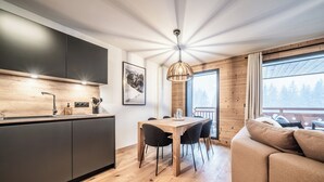 A modern kitchen with dark cabinets, a wooden dining table, and a large window overlooking a forest. - Gentiana - Cosy apartment in Les Gets (Les Gets)