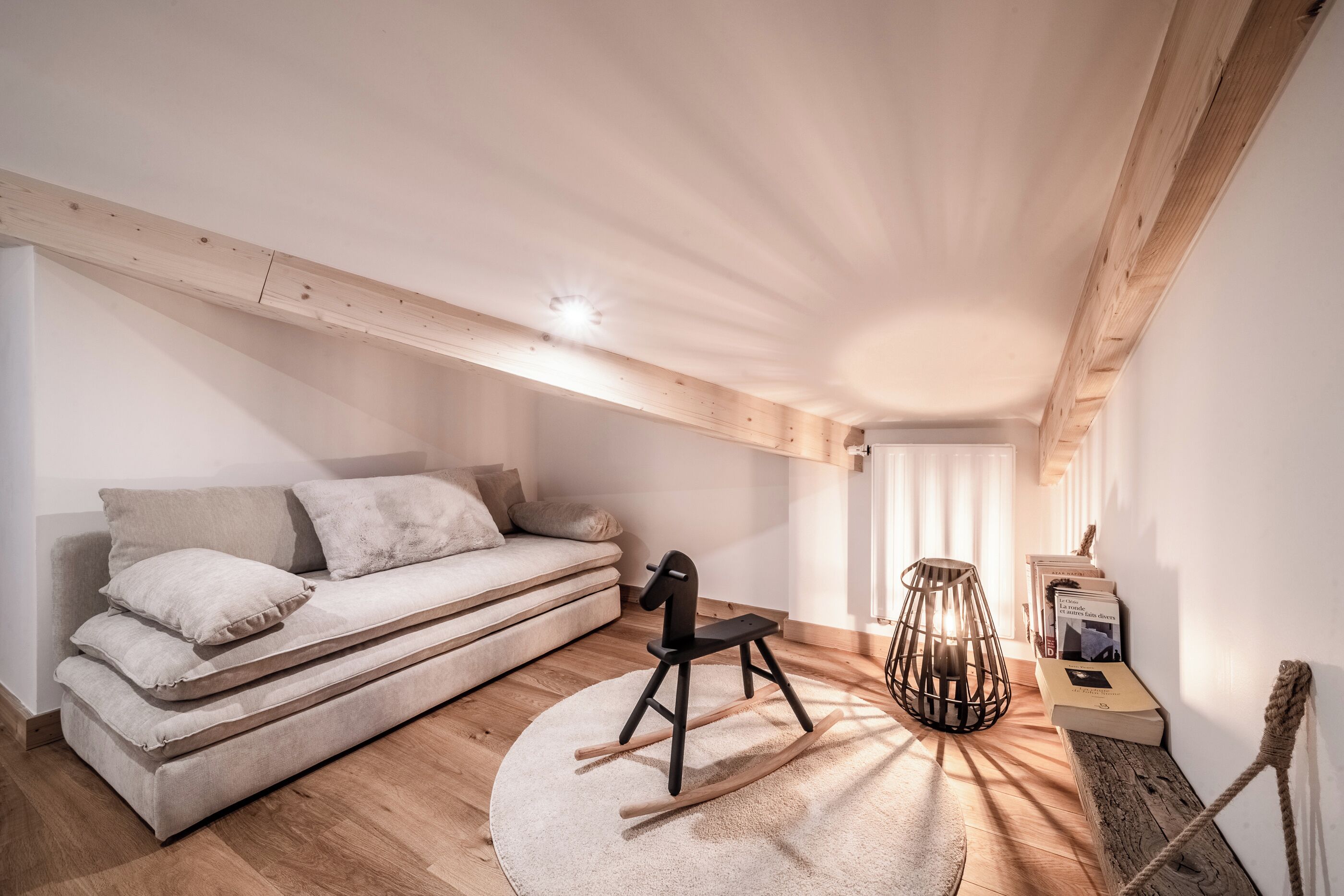 Een moderne loft slaapkamer met een ingebouwde bank, een schommelstoel, een houten vloer en een schuin dak met zichtbare balken.