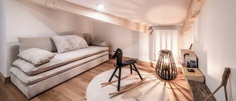Een moderne loft slaapkamer met een ingebouwde bank, een schommelstoel, een houten vloer en een schuin dak met zichtbare balken.
