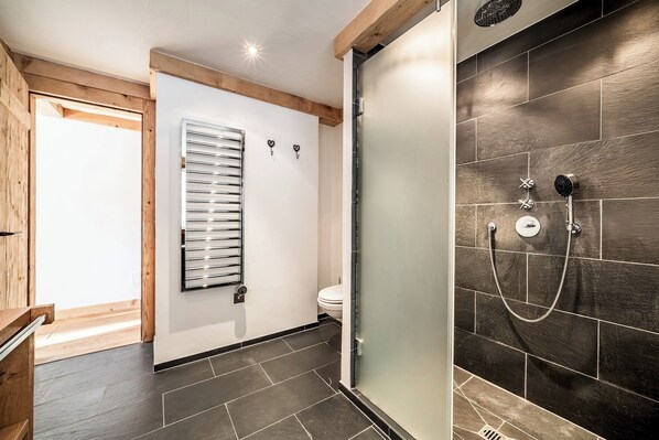 A modern bathroom with a glass shower enclosure, a toilet, and a window with blinds. - Snowcrest - Cosy Apartment in the heart of Verbier (Verbier)