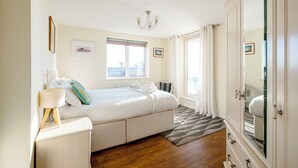 Un dormitorio con cama, mesita de noche, lámpara, ventana con cortinas, espejo y vistas al exterior.