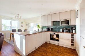 A modern kitchen with white cabinetry, a wooden countertop, a built-in oven, and a microwave.