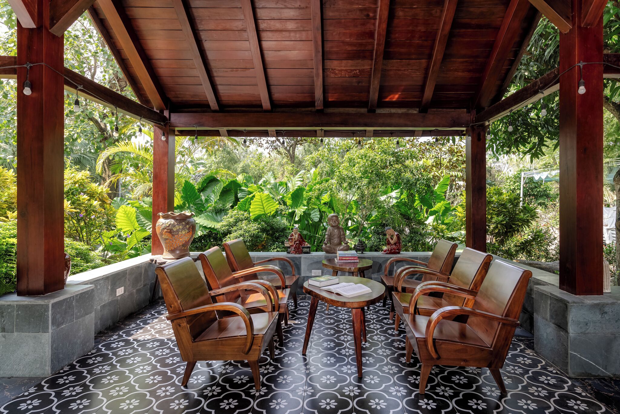An outdoor seating area with wooden chairs and a table, surrounded by a tiled floor and a wooden pergola.