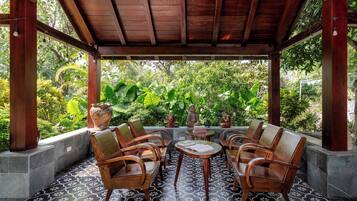 An outdoor seating area with wooden chairs and a table, surrounded by a tiled floor and a wooden pergola.