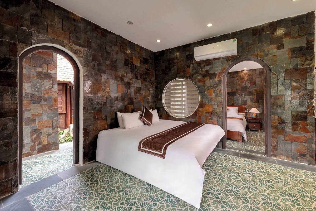 Una habitación de hotel moderna con una cama grande, paredes de piedra, un espejo redondo y un piso con diseño.
