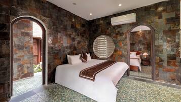 A modern hotel room with a large bed, stone walls, a round mirror, and a patterned floor.