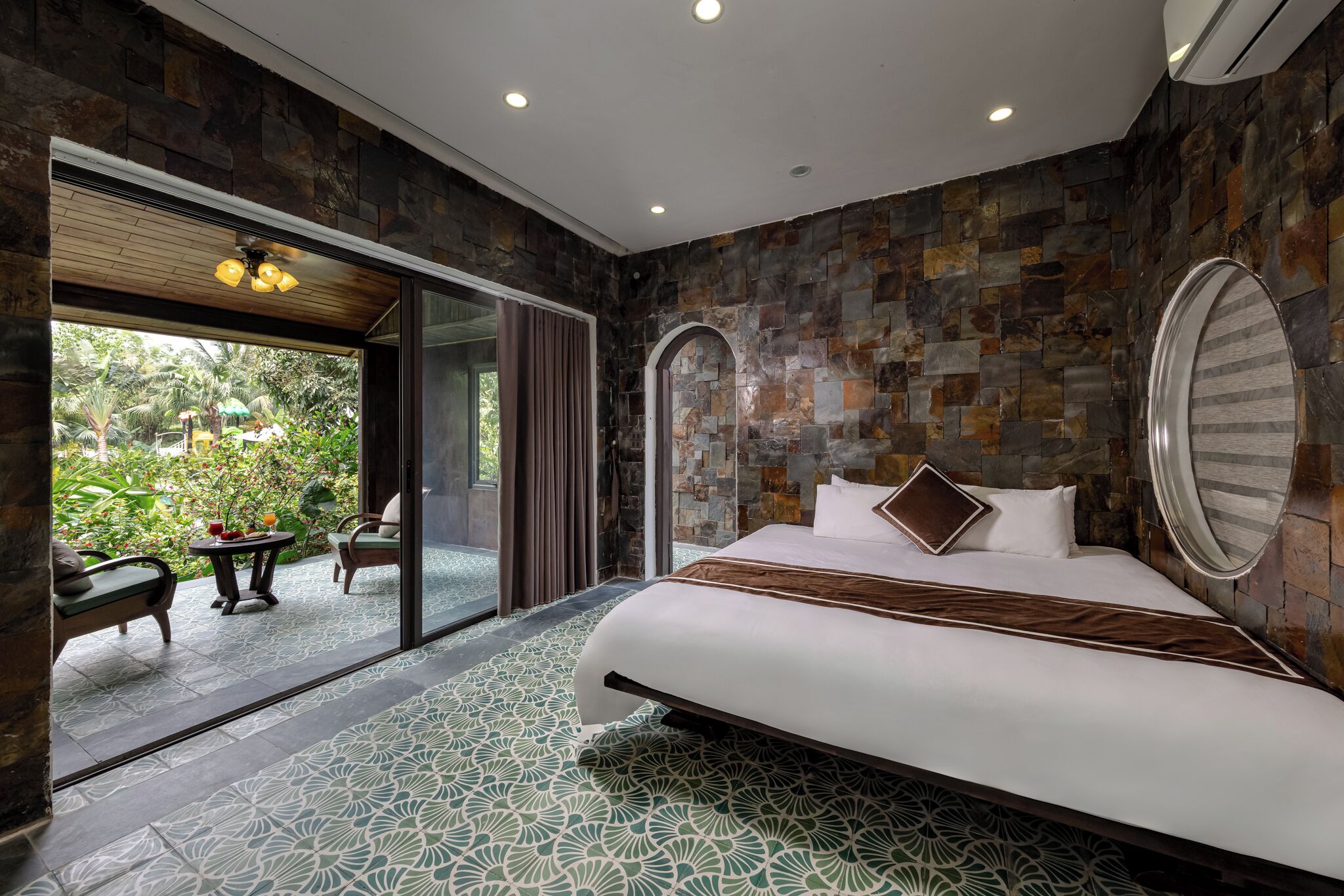 A bedroom with a large bed, a glass door leading to an outdoor area, and a stone wall.