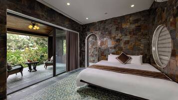 A bedroom with a large bed, a glass door leading to an outdoor area, and a stone wall.