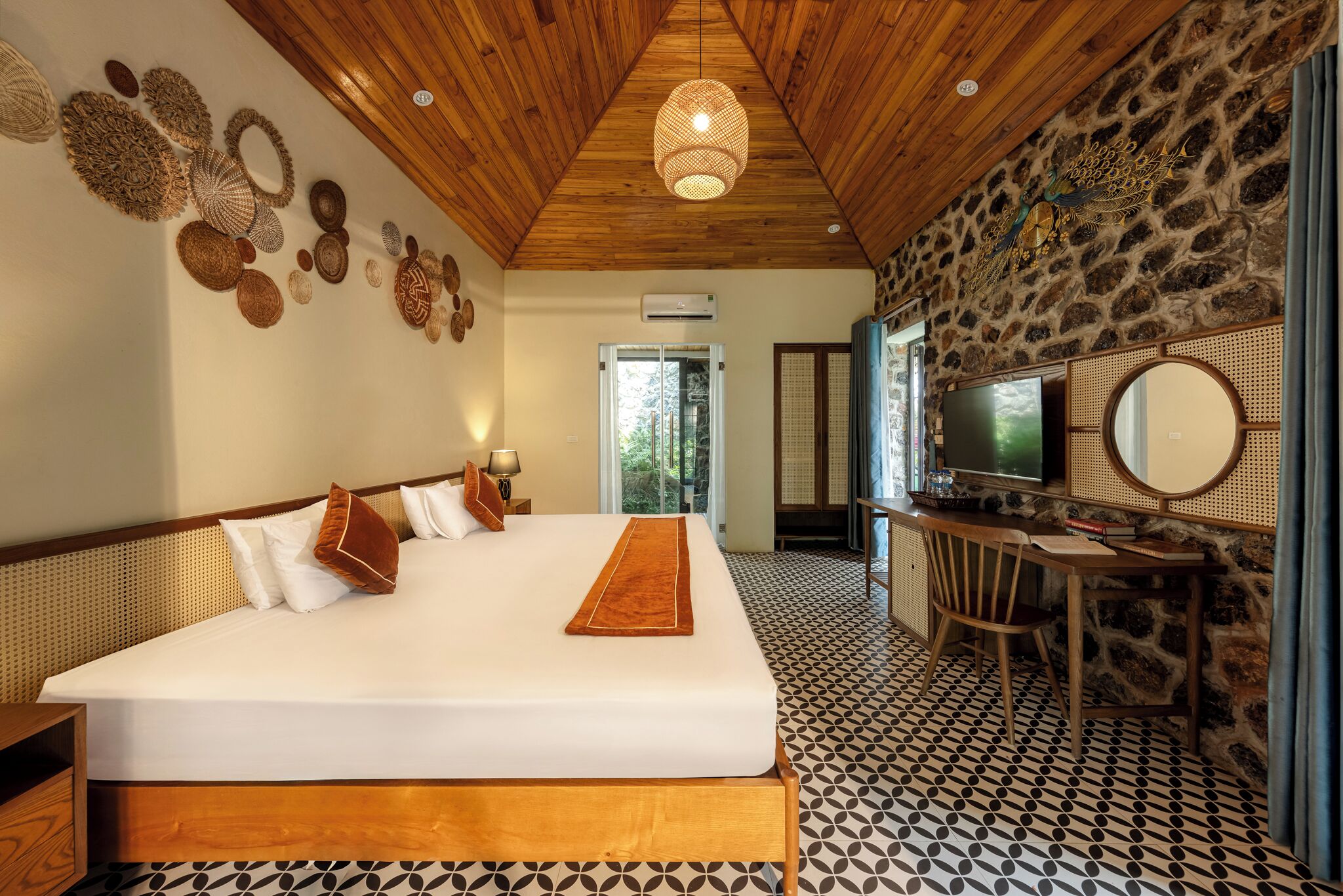 A bedroom with a large bed, a desk with a TV, and a stone wall.