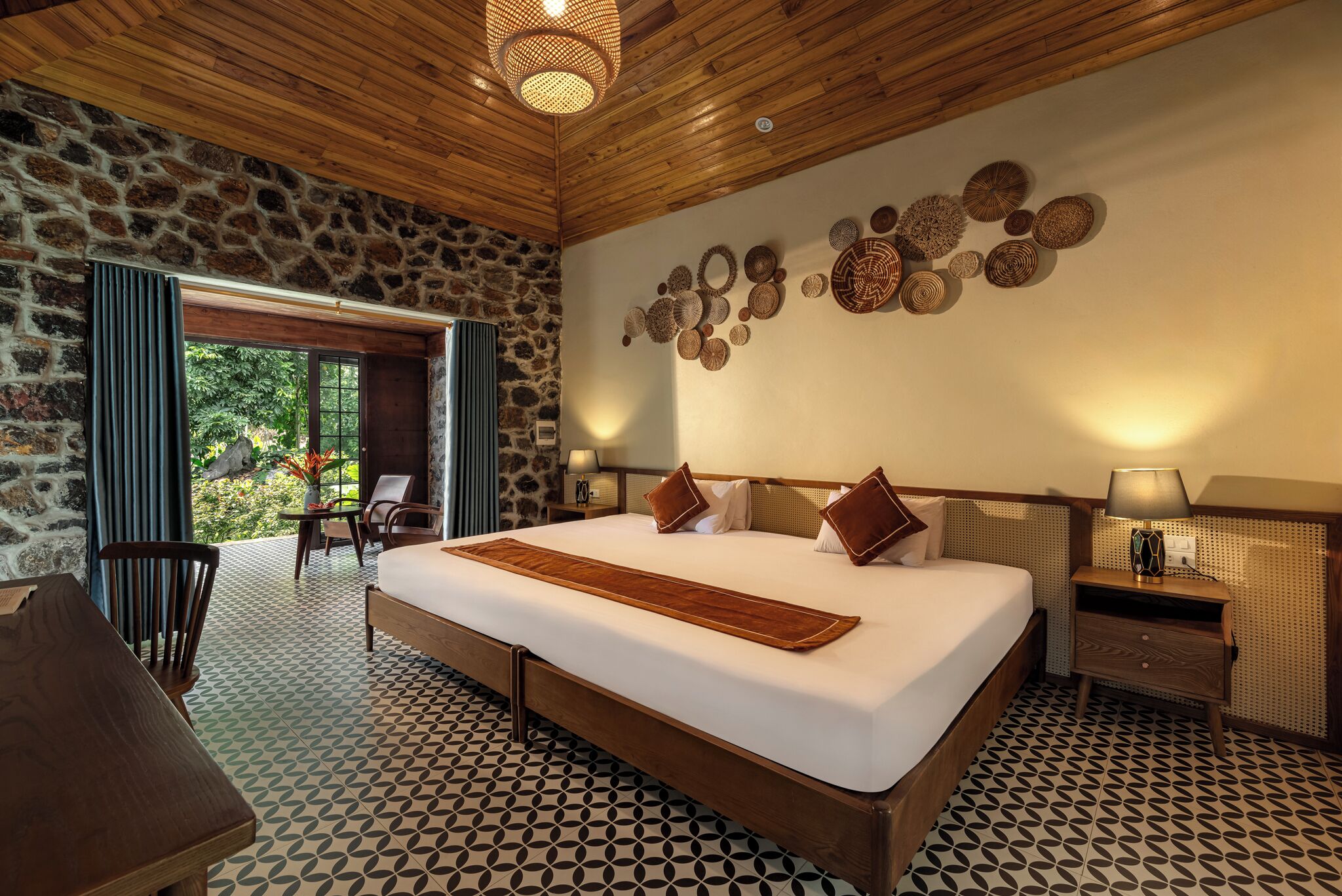 A spacious bedroom with a large bed, a stone wall, and a view of greenery.